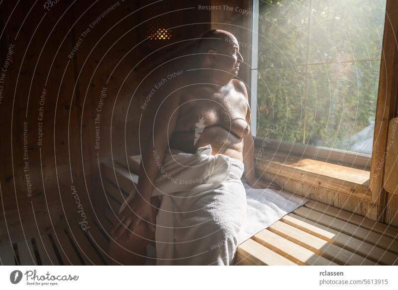Mann sitzt in einer sonnigen finnischen Sauna, schaut aus dem Fenster und ist in ein Handtuch gewickelt Wellnessbad Resort Hotel Schweiß Finnland Finnisch