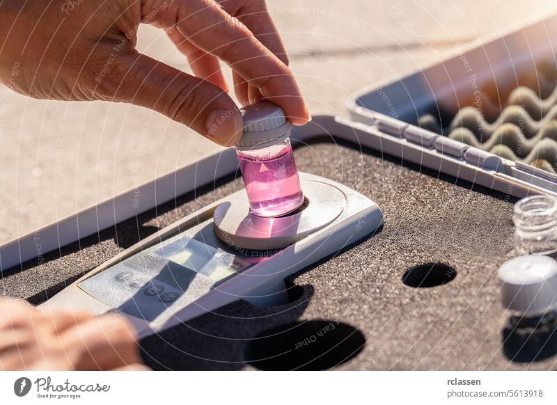 Hand, die eine rosa Flüssigkeitsflasche auf ein digitales Analysegerät in einem Testkit stellt chemische Analyse Labor Wasserqualität ph-Testkit Lösungsmittel