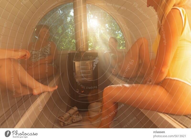 Drei Frauen genießen einen Saunagang, Sonnenstrahl durch Fenster, Ofen mit Brennholz Erholung Wellness Gesundheit Spa erwärmen Holzofen Sonnenstrahlen