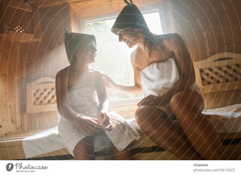 Mutter und Kind lächeln sich in einer finnischen Sauna an, beide tragen Filzhüte Bademantel Verdunstung Spa-Wellness Hotel Windstille Tochter Familie Frau
