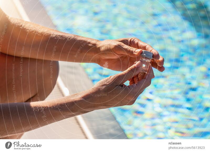 Hände, die ein kleines Fläschchen mit Wasser für pH-Tests in der Nähe eines Schwimmbeckens schließen, in dem sich das Sonnenlicht auf der Oberfläche spiegelt