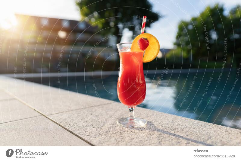 erfrischender roter Cocktail garniert mit einer Erdbeer- und Orangenscheibe am Pool bei Sonnenuntergang Wellness Spa Hotel Beckenrand rotes Getränk