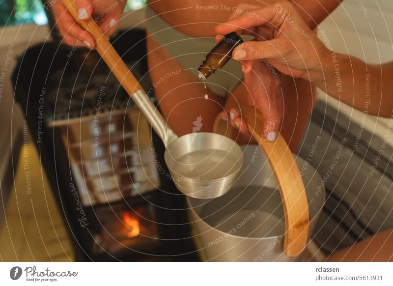 Nahaufnahme von Händen, die ätherisches Öl in eine Saunakelle über einen Eimer gießen. Finnische mobile Sauna Konzeptbild Aroma Aromatherapie Badeanzüge