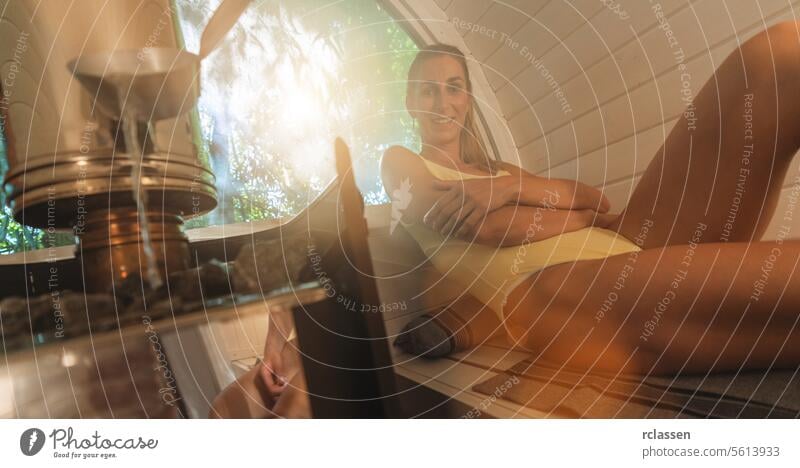 Entspannte Frau sitzt in einer Sauna, Wasser wird auf heiße Steine im Vordergrund gegossen. Mobile Finish Sauna Konzept Bild Wasser gießen Erholung Wellness