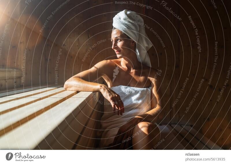Frau in einer finnischen Sauna, auf einen Arm gestützt, ein Handtuch um den Kopf gewickelt, Sonnenlicht in einem Wellness-Spa-Hotel vihta Wellnessbad Resort