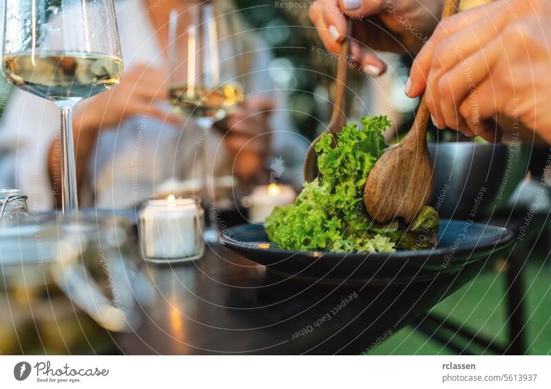 Nahaufnahme eines Salats, der mit Holzutensilien serviert wird, mit Weingläsern und Kerzen im Hintergrund Salatbeilage Servieren Gesunde Ernährung frisch