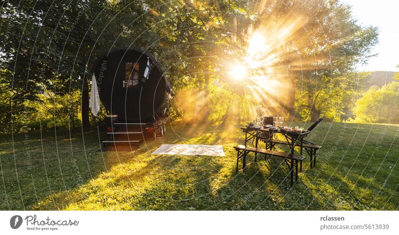 Sonnenstrahlen über einem finnischen Mobiel-Saunafass und einem gedeckten Tisch auf einer üppigen Wiese Resort Hotel Fahne Amuse-Gueule Wein Holzfass