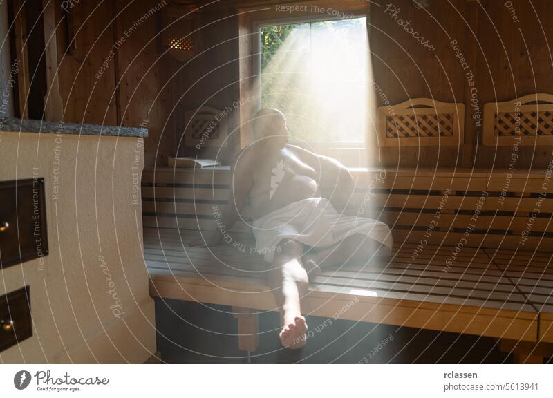 Ein Mann sitzt in einer Sauna und das Licht fällt durch das Fenster auf seine entspannte Figur. Wellnessbad Resort Hotel Schweiß Finnland Finnisch