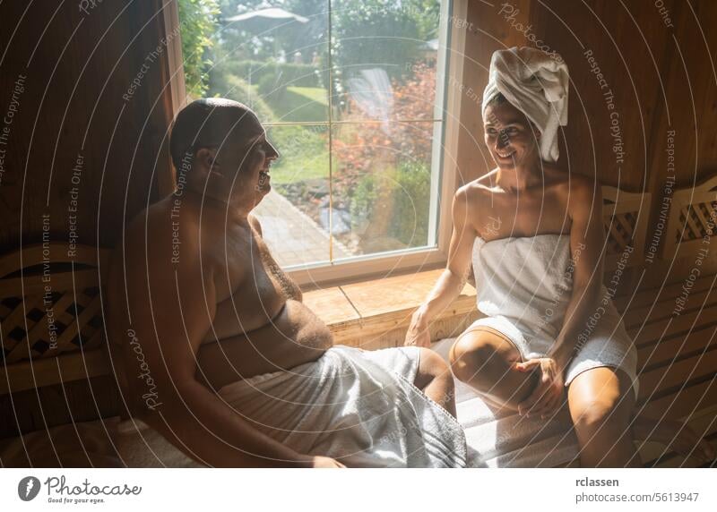 Mann und Frau in einer Sauna, Frau mit einem Handtuch auf dem Kopf, beide lächelnd und sitzend im Wellness-Hotel Wellnessbad Resort Fenster Schweiß Finnland