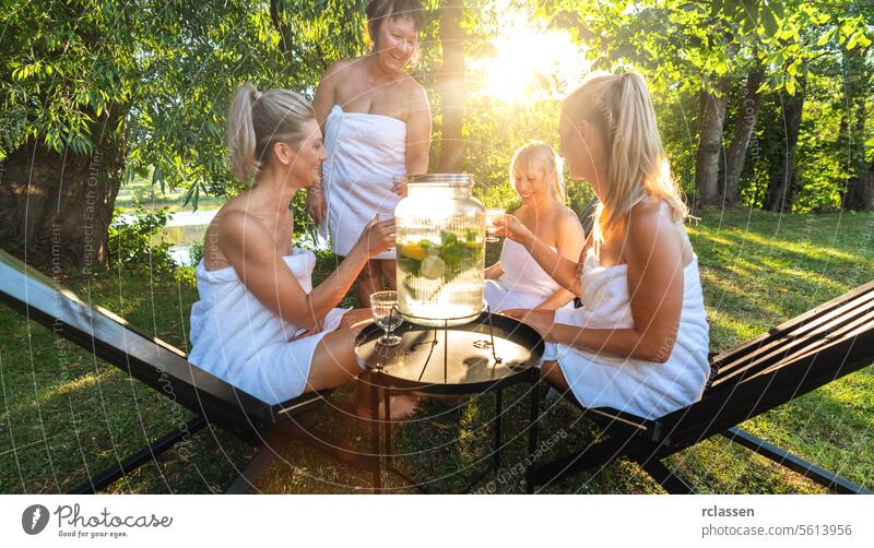 Gruppe von Frauen in weißen Handtüchern, die nach der finnischen Sauna in einem Park aufgegossenes Wasser mit Zitronen genießen Minze Kalk Frauengruppe