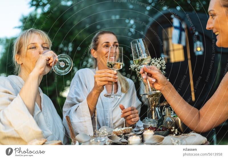 Freunde in Bademänteln stoßen mit Weißwein neben einem Saunafass im Freien an Röstung Außeneinstellung Genuss Erholung Wellness Natur Spa Gesundheit Freizeit