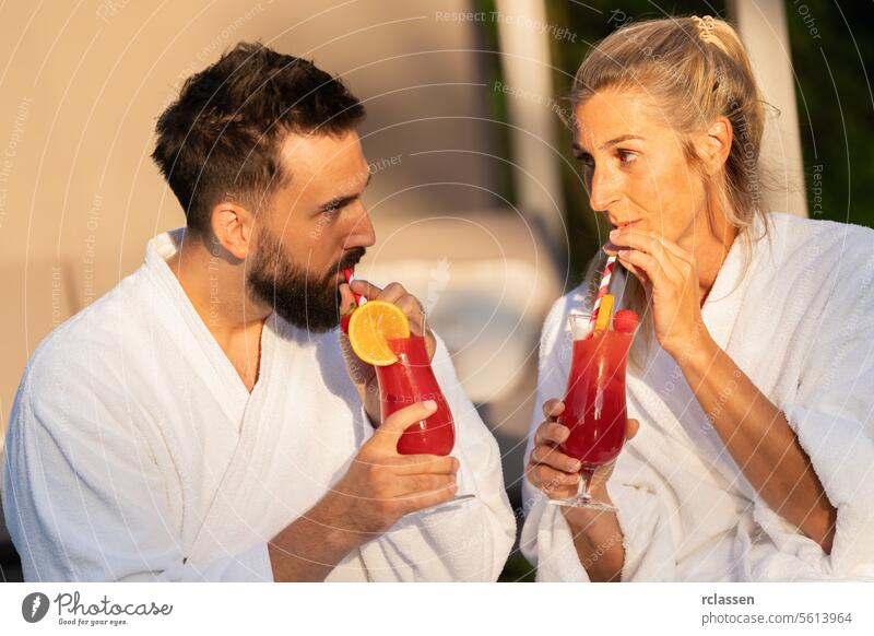 Paar in weißen Bademänteln trinkt Cocktails und schaut sich in einem Hotel an schlürfend Bademantel Wellness Spa-Wellness-Resort weiße Gewänder rote Cocktails