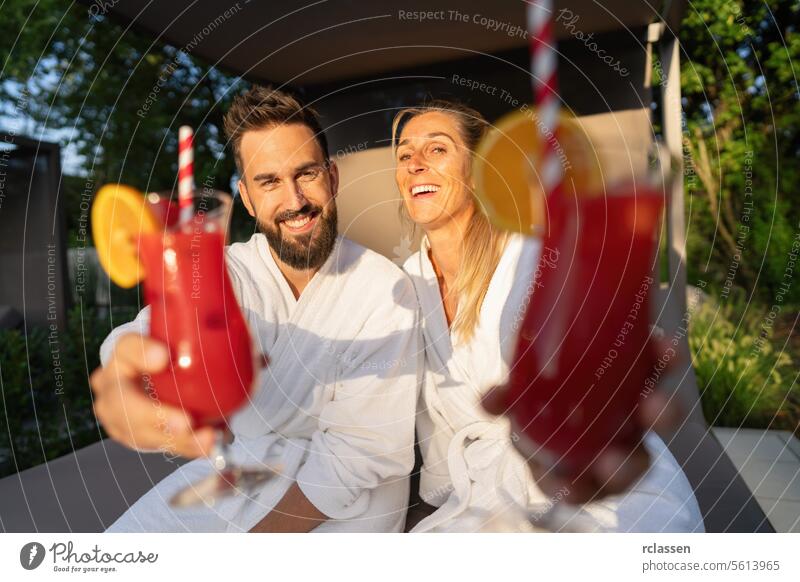 Fröhliches Paar in weißen Bademänteln genießt rote Cocktails in einem Wellness-Resort Bademantel Hotel Spa-Wellness-Resort weiße Gewänder freudig Erholung