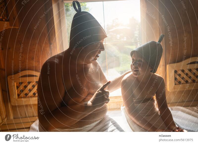 Vater und Tochter in der finnischen Sauna, mit Filzhüten, der Vater spricht und die Tochter hört zu. Hotel Zeigen Schweiß Finnisch sprechend hören Holzbank