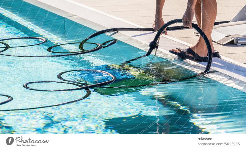 Person, die einen Schlauch eines Schwimmbecken-Reinigungsroboters am Rande eines Schwimmbeckens benutzt Frau Dienstleistungsbranche Technikeruniform Poolpflege