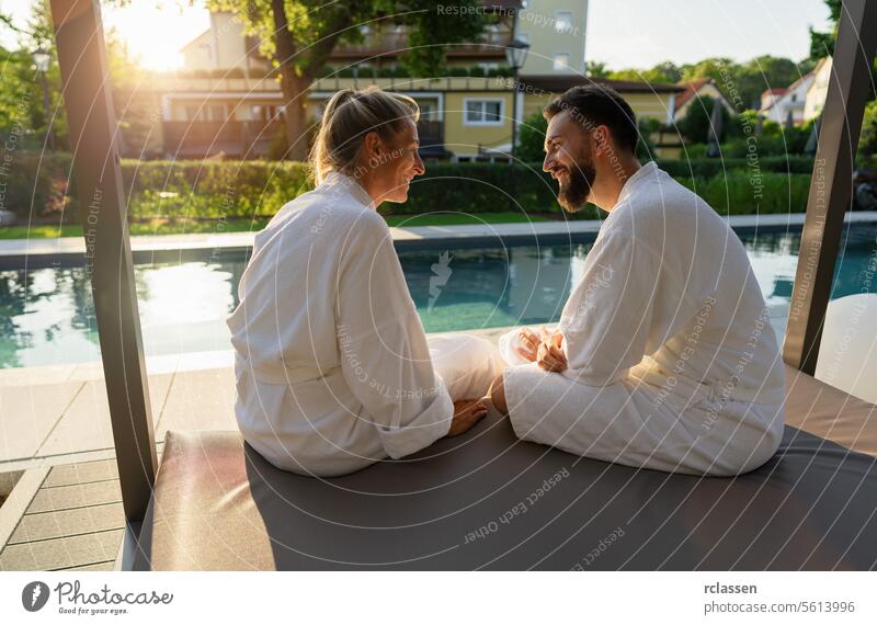 Paar in weißen Bademänteln genießt den Sonnenuntergang am Pool in einem Wellness-Hotel Resort Liebe weiße Gewänder Erholung Freizeit Genuss Spa im Freien