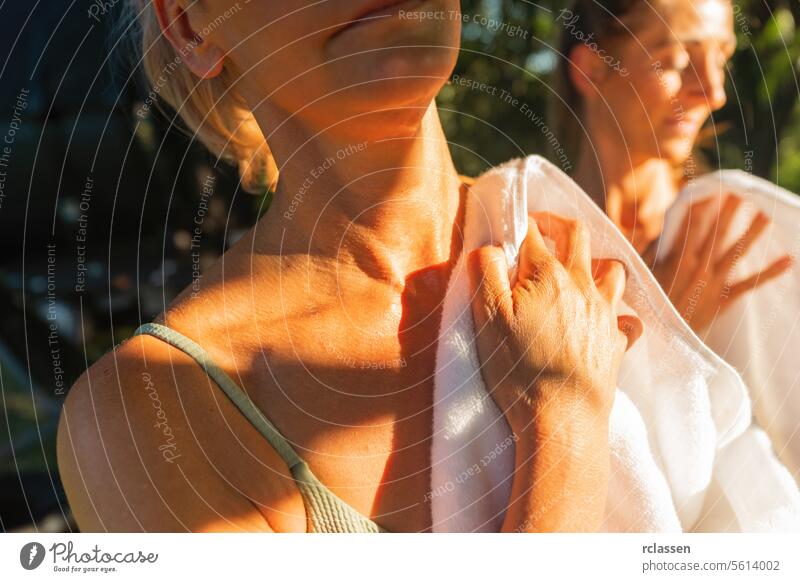 Nahaufnahme von zwei Frauen, die sich nach der finnischen Sauna mit Handtüchern im Sonnenlicht abtrocknen Finnisch Abtrocknen Spa Wellness Erholung Freizeit