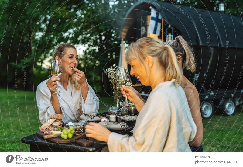 Freunde genießen Snacks und Wein in der Nähe eines Saunafasses in einer üppigen Außenanlage Frau Nebel Außeneinstellung üppig (Wuchs) Genuss Erholung Wellness