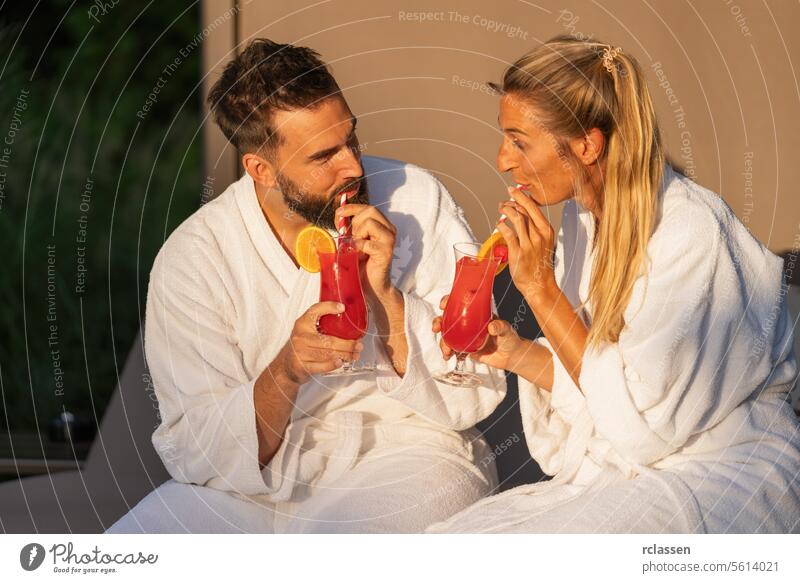 Mann und Frau in weißen Gewändern schlürfen Cocktails im Licht der goldenen Stunde im Wellness-Hotel-Resort schlürfend Bademantel Spa-Wellness-Resort Paar