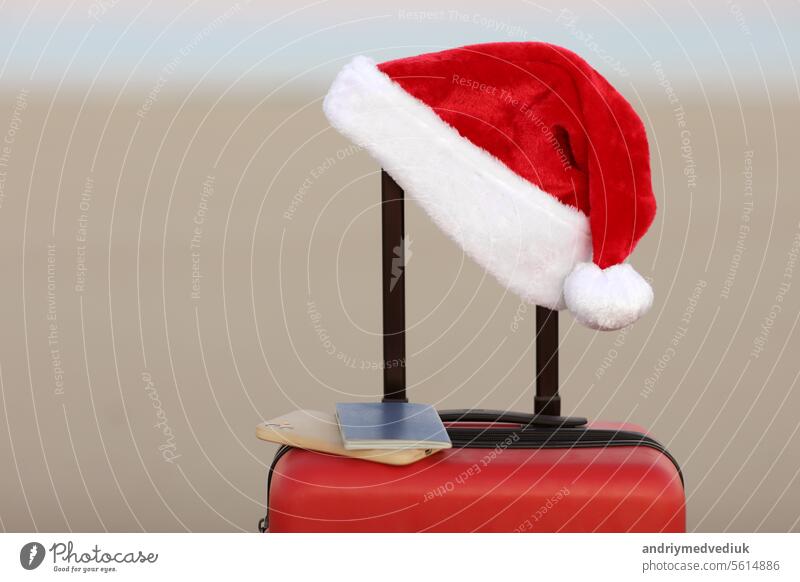 Weihnachtsmann-Mütze, Smartphone und Reisepass auf rotem Koffer auf Meeresstrand Sandstrand. Reisen auf Weihnachten und Neujahr Winterferien Konzept. Last-Minute-Reisen, heiße Touren. Kopierraum für Werbung
