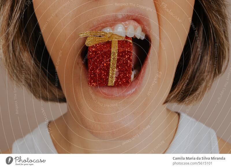 Nahaufnahme eines weiblichen Mundes, der in einen geschenkförmigen Weihnachtsschmuck beißt. Einstellung schön Schönheit hell Farbe Konzept Detailaufnahme essen