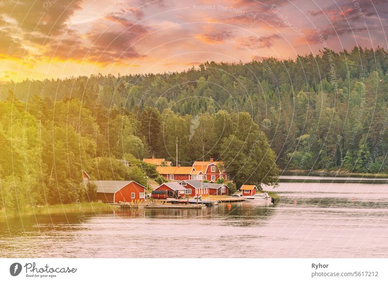 Schweden. Schöne rote und gelbe schwedische Holzblockhütten Häuser auf felsigen Insel Küste im Sommer Abend. See oder Fluss Landschaft. Sonnenuntergang Sommerhimmel mit Sonnenlicht Sonnenschein. verändert Sonnenaufgang Himmel.