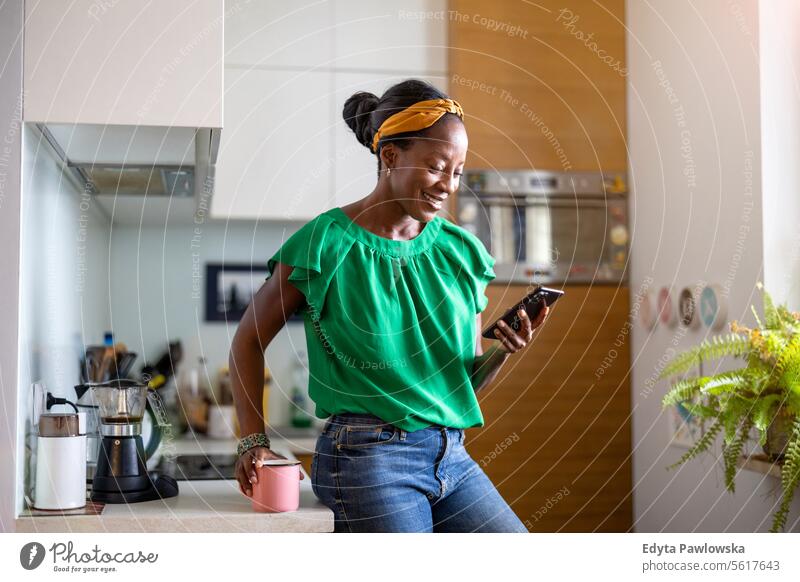 Reife Frau benutzt Smartphone in der Küche zu Hause Menschen Freude schwarz natürlich attraktiv schwarze Frau Fröhlichkeit Glück echte Menschen reif Erwachsener