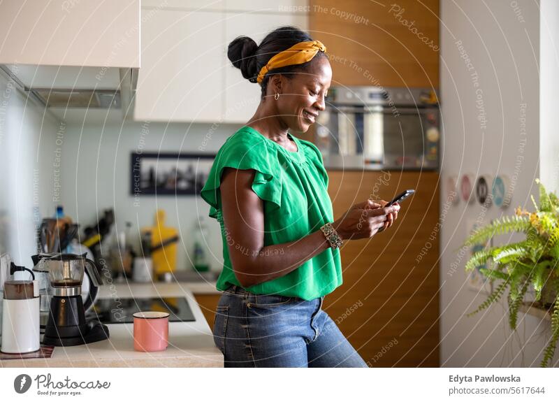 Reife Frau benutzt Smartphone in der Küche zu Hause Menschen Freude schwarz natürlich attraktiv schwarze Frau Fröhlichkeit Glück echte Menschen reif Erwachsener