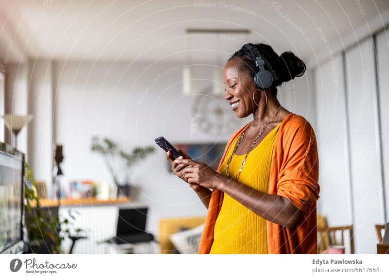 Frau hört Musik mit Kopfhörern, die an ihr Smartphone angeschlossen sind, im heimischen Wohnzimmer Menschen Freude schwarz natürlich attraktiv schwarze Frau