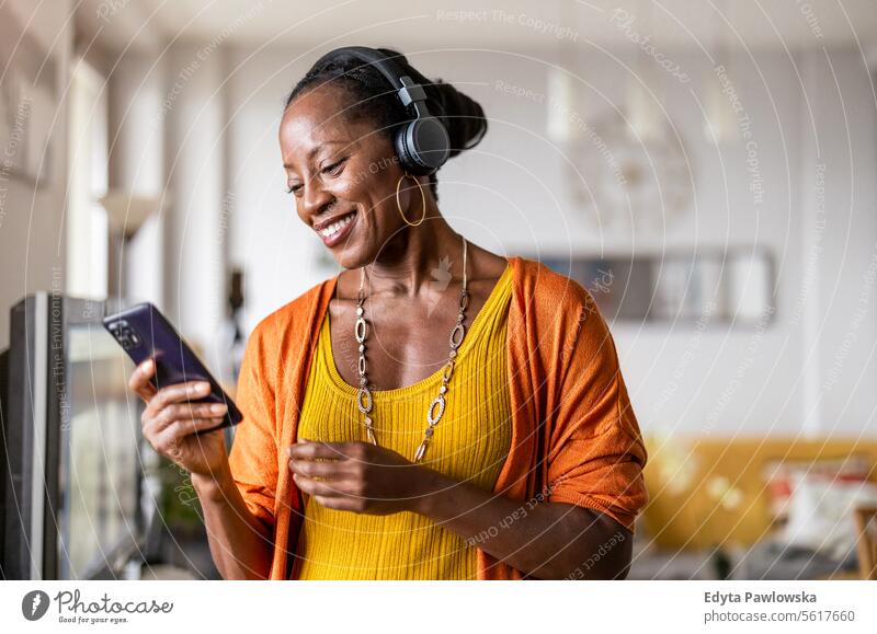 Frau hört Musik mit Kopfhörern, die an ihr Smartphone angeschlossen sind, im heimischen Wohnzimmer Menschen Freude schwarz natürlich attraktiv schwarze Frau