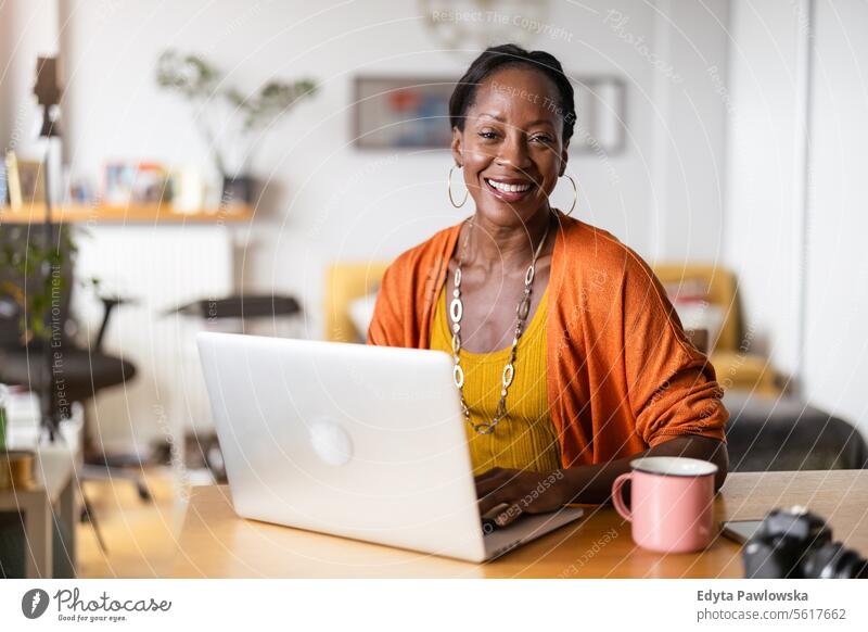 Lächelnde Frau, die zu Hause an ihrem Laptop arbeitet Menschen Freude schwarz natürlich attraktiv schwarze Frau Fröhlichkeit Glück echte Menschen reif