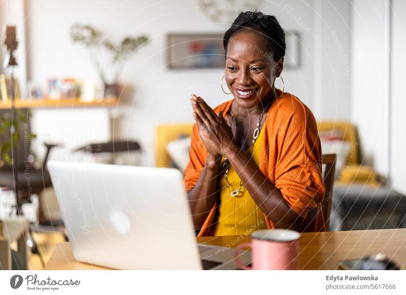 Lächelnde Frau arbeitet zu Hause am Laptop Menschen Freude schwarz natürlich attraktiv schwarze Frau Fröhlichkeit Glück echte Menschen reif Erwachsener