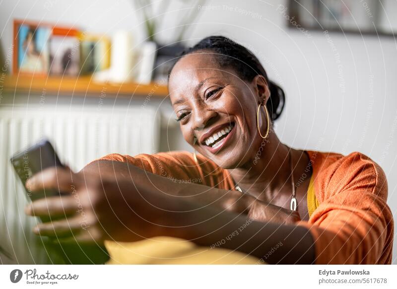Reife Frau, die ein Mobiltelefon benutzt, während sie sich zu Hause auf dem Sofa entspannt Menschen Freude schwarz natürlich attraktiv schwarze Frau