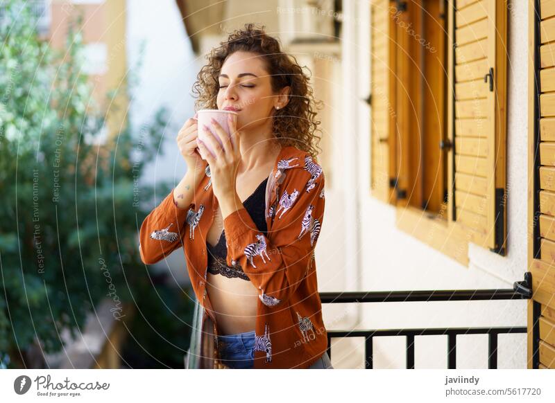 Junge Frau genießt einen Kaffee auf dem Balkon eines Hauses genießen Tee krause Haare Gebäude frisch modern Vergnügen Dame trinken Heißgetränk brünett Straße