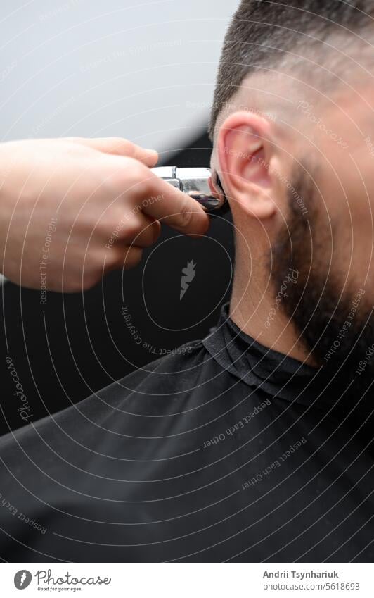 Der Friseur rasiert die Schläfe mit einem kabellosen Trimmer bei einem Kurzhaarschnitt an den Seiten des Kopfes. Rasierer Mann elektrisch Rasur kahl