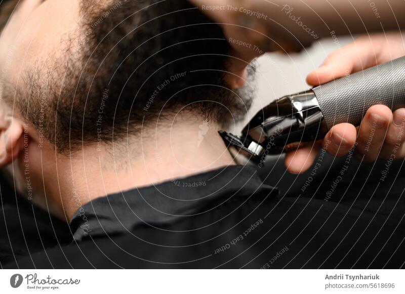 Ein Friseur im Salon trimmt den Bart eines Mannes mit einem Trimmer im Nackenbereich Hals Vollbart Schermaschine Arbeit Barbershop Kopf Haarschnitt jung Klient