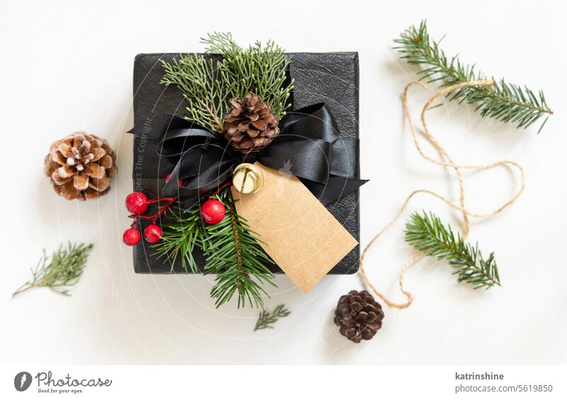 Schwarzes Weihnachtsgeschenk mit leerem Geschenkanhänger, mit Tannenzweig und Dekorationen, Mockup Weihnachten Attrappe präsentieren Postkarte schwarz