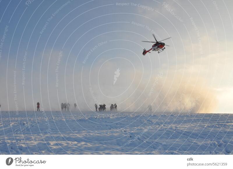 Wie aus dem Nichts erscheint plötzlich ein Helikopter der Luftrettung am Himmel und hüllt die Menschen beim Landen in einen Wirbel aus Neuschnee. Hubschrauber