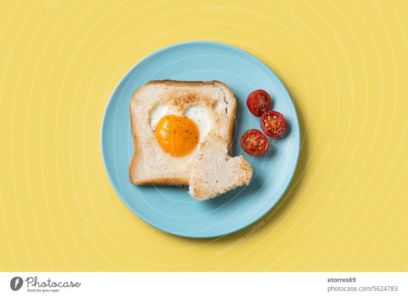 Valentinstag Frühstück mit Ei mit Tomaten, herzförmig und Toastbrot auf gelbem Hintergrund blau Brot Konzept Lebensmittel gebraten Gesundheit Herz vereinzelt