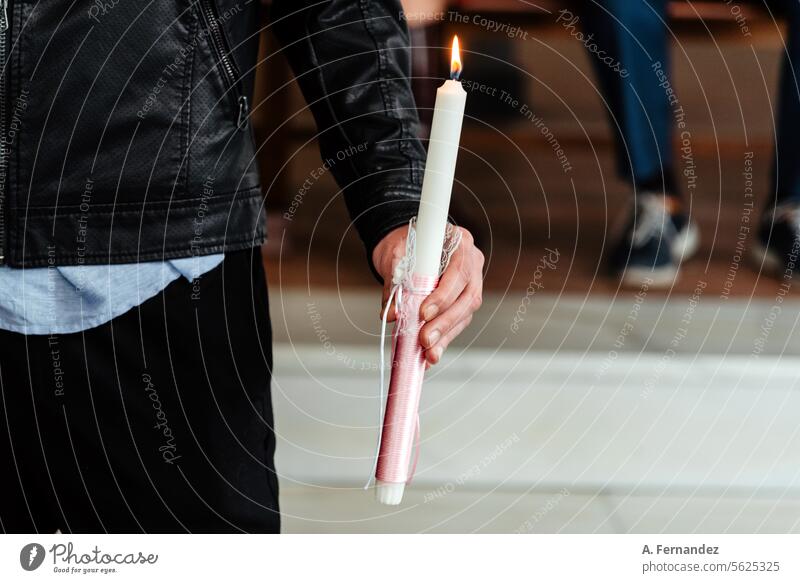 Detail einer männlichen Hand, die eine brennende Kerze in der Kirche hält. Konzept des Sakraments der christlichen Taufe. Brennende rosa Taufkerze. Taufbecken