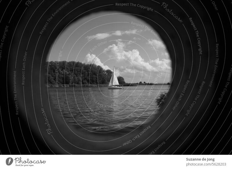 Schwarz-Weiß-Bild eines Segelboots auf einem See mit bewölktem Himmel, betrachtet durch ein (gefälschtes) Fernglas Segeln Schiff wolkig Wasser Boot Segelschiff