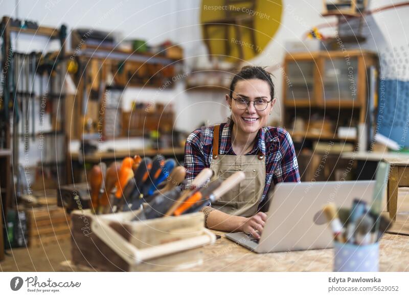 Junge Handwerkerin mit Laptop in ihrer Werkstatt Möbel Zimmerer wiederherstellend Schreinerei Holz Stuhl Gebäude Inszenierung Renovierung reparierend Nutzholz