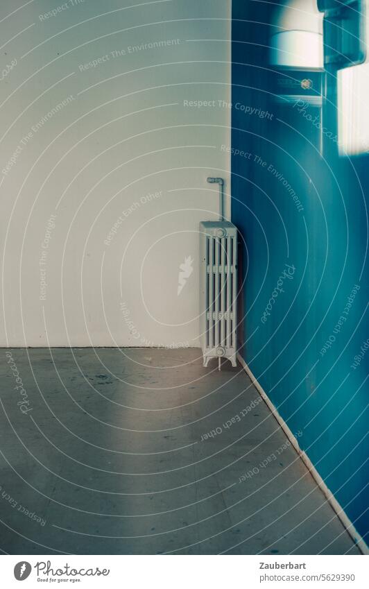 Eine Heizung in der Ecke eines leeren Raumes mit weißen und blauen Wänden sowie grauem Estricht Wand Winkel geometrisch Heizkörper Heizkosten Radiator heizen