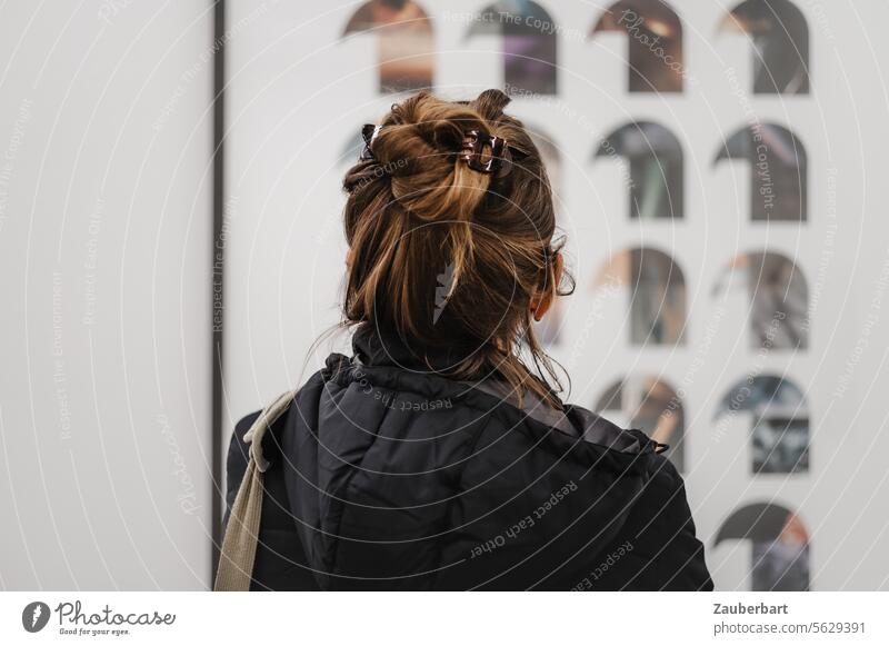 Besucherin im Museum betrachtet Kunst, Kopf einer Frau von hinten, Kapuze betrachten Frisur Ansicht hochgesteckt Rückansicht Jacke Haare versunken aufmerksam
