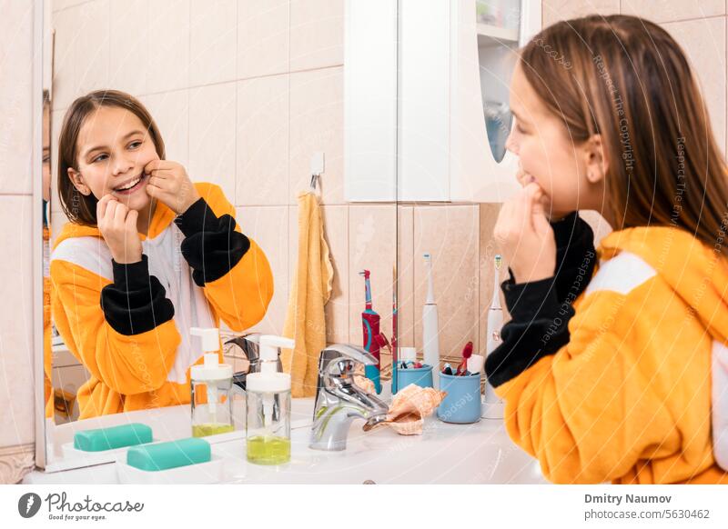 Mädchen in orangefarbenem Schlafanzug verwendet Zahnseide, um Plaque zwischen den Zähnen zu entfernen Gesunder Lebensstil Pyjama Bad Schlafenszeit Pflege Karies