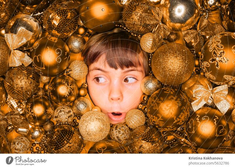 Überrascht kleiner Junge Gesicht mit Freude in goldenen Weihnachtsbaum Spielzeug Kugeln. Feiertag. Ball Kind Neujahr Kinder Dekoration & Verzierung heimwärts