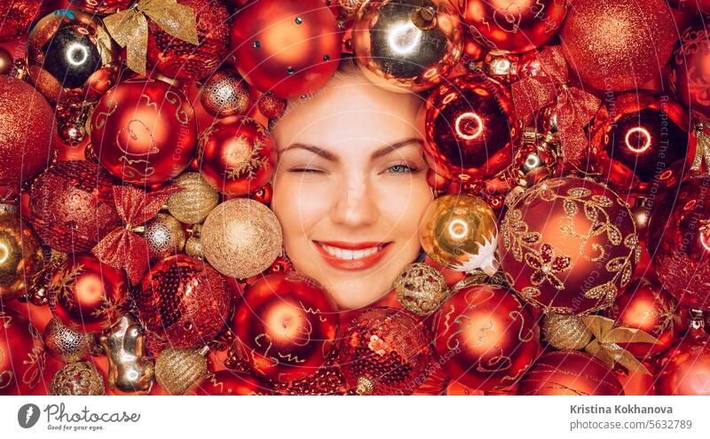 Glückliche Frau blinzelte mit Freude Lächeln in roten Weihnachtsbaum Spielzeug Kugeln. Feiertage. Ball Neujahr Dekoration & Verzierung heimwärts Ornament