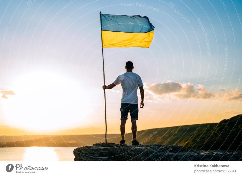 Ukrainischer Mann mit Nationalflagge am Sommerhimmel, hoher Fels, breiter Fluss Dnjestr Fahne Ukraine Krieg Konflikt Freiheit Selbstständigkeit Ukrainer Armee