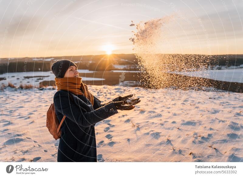 Eine Frau im Winter in warmer Kleidung wirft ihre Palmen und Schnee vor dem Hintergrund des Sonnenuntergangs warme Kleidung werfen Handfläche Menschen Person