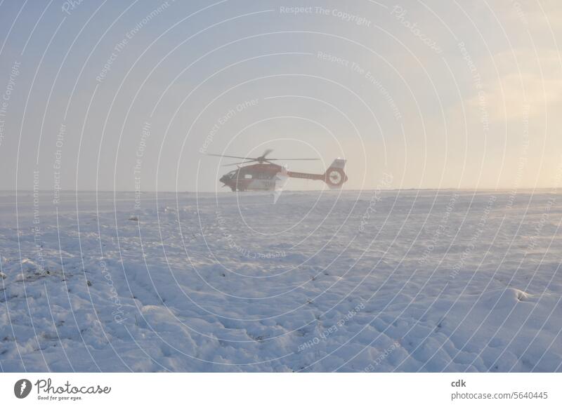 Ein Helikopter der Luftrettung ist am Berg gelandet. Der aufgewirbelte Neuschnee legt sich langsam und taucht die Szene in ein sanftes Licht. Hubschrauber